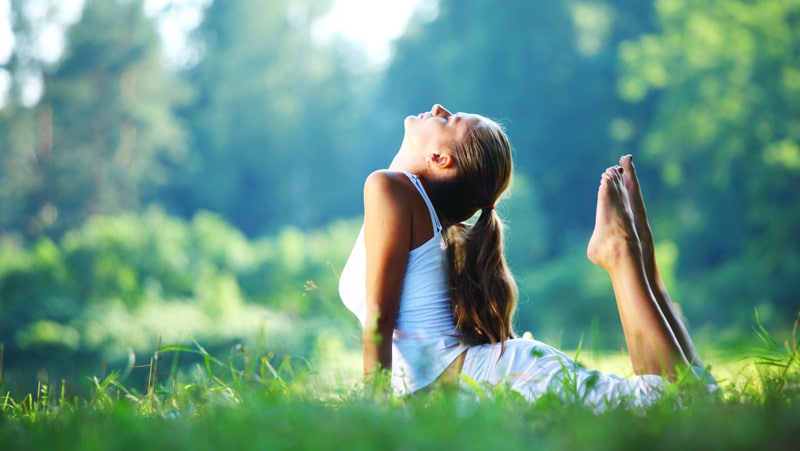 Frau macht Yoga im Freien auf einer Wiese, entspannt bei sonnigem Wetter.