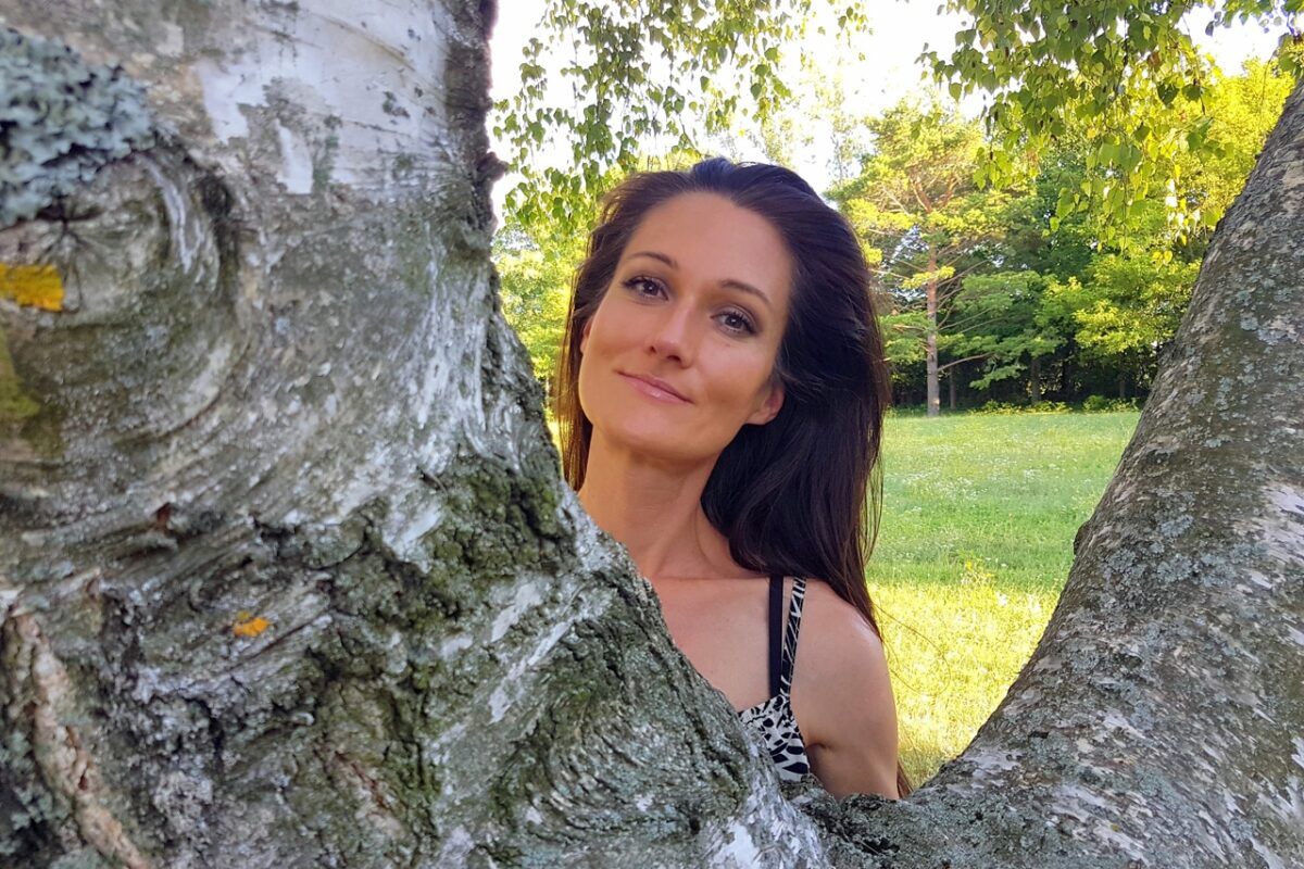 Eine Frau blickt zwischen Baumstämmen hindurch in einem sonnigen Park.