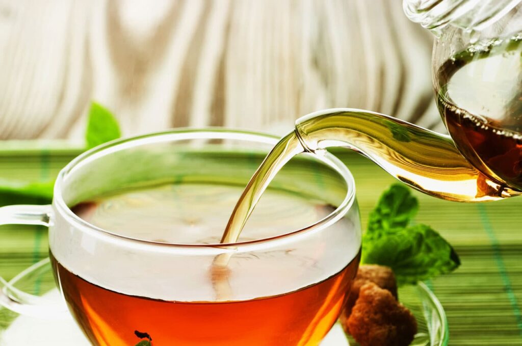 Eine durchsichtige Tasse Tee, die aus einer Teekanne befüllt wird